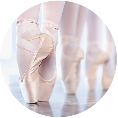 Stopy kilku baletnic stojących na czubkach palców na scenie. Zdjęcie w barwach jasnoróżowych i cielistych.